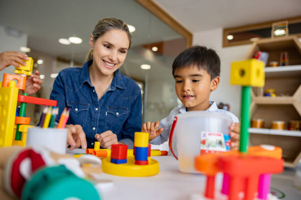 Happy Latin American schoolboy playing with building blocks in the classroom and the supervision of his teacher