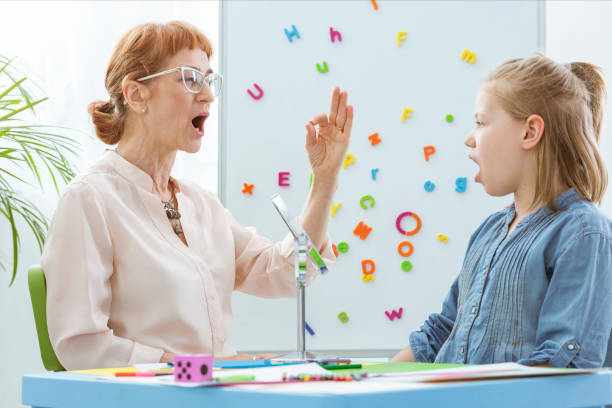 Special education teacher working with little girl during speech therapy